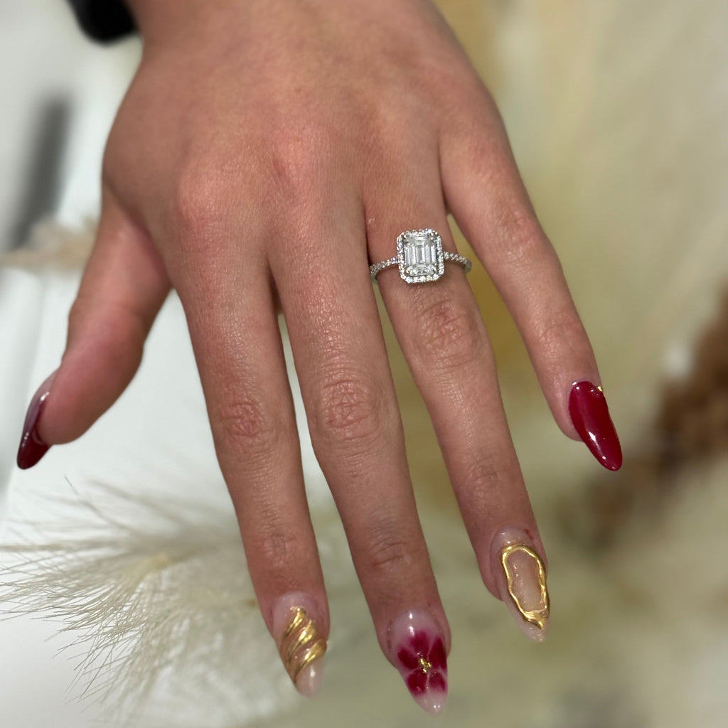 Close-up of a hand wearing a diamond ring with red and gold nail polish.