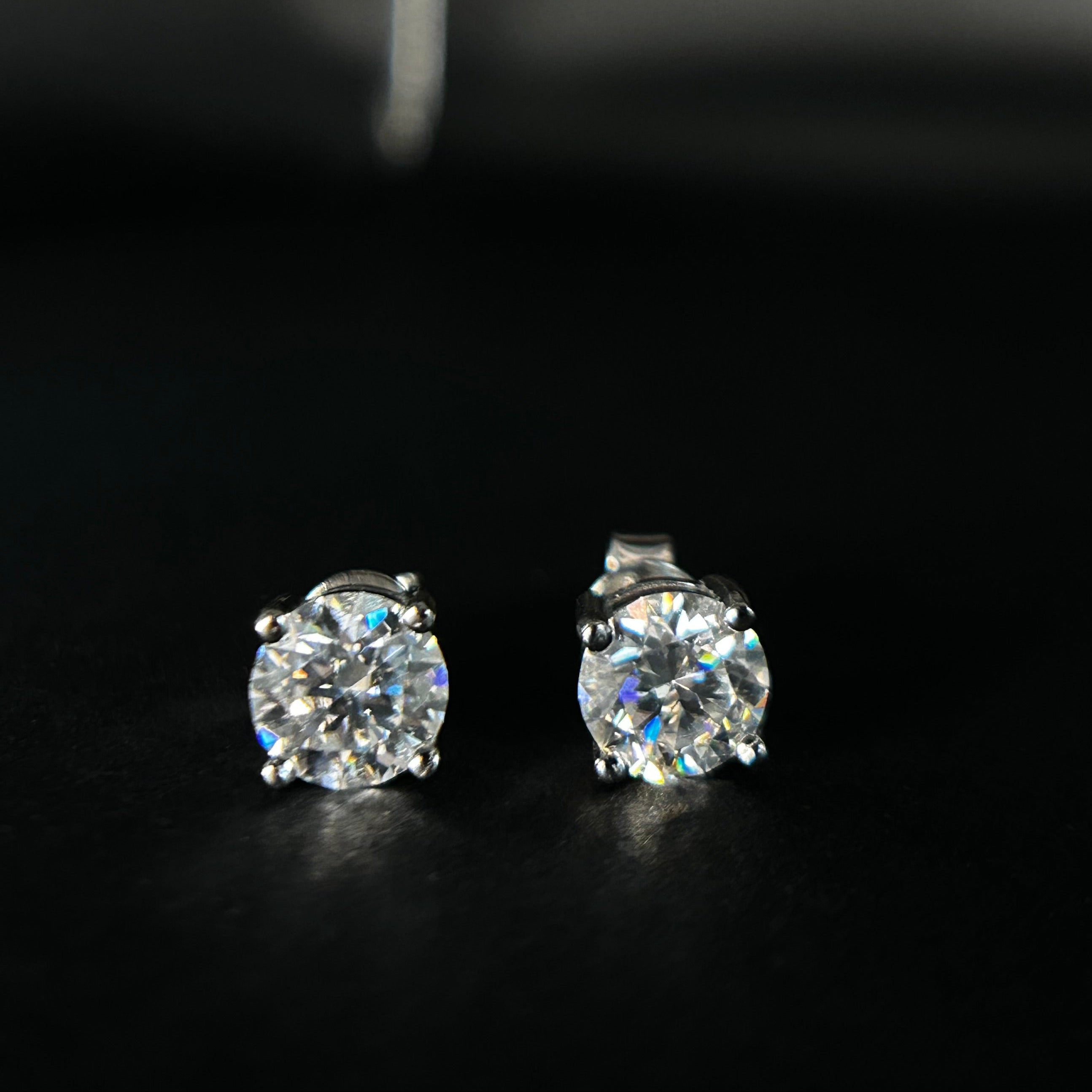 Two diamond stud earrings on a dark background