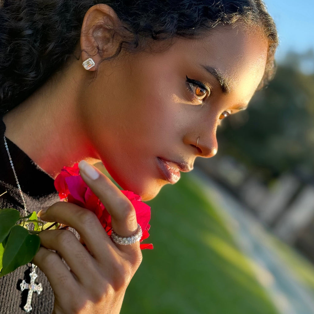 Model holding a Pink flower wearing a cross necklace and earrings from Lea Fine Jewelry